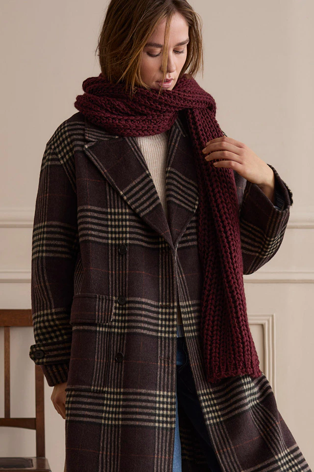 Model trägt einen dunkelbraunen karierten Mantel mit burgunderfarbenem Schal, Jeans und braunen Loafern.
