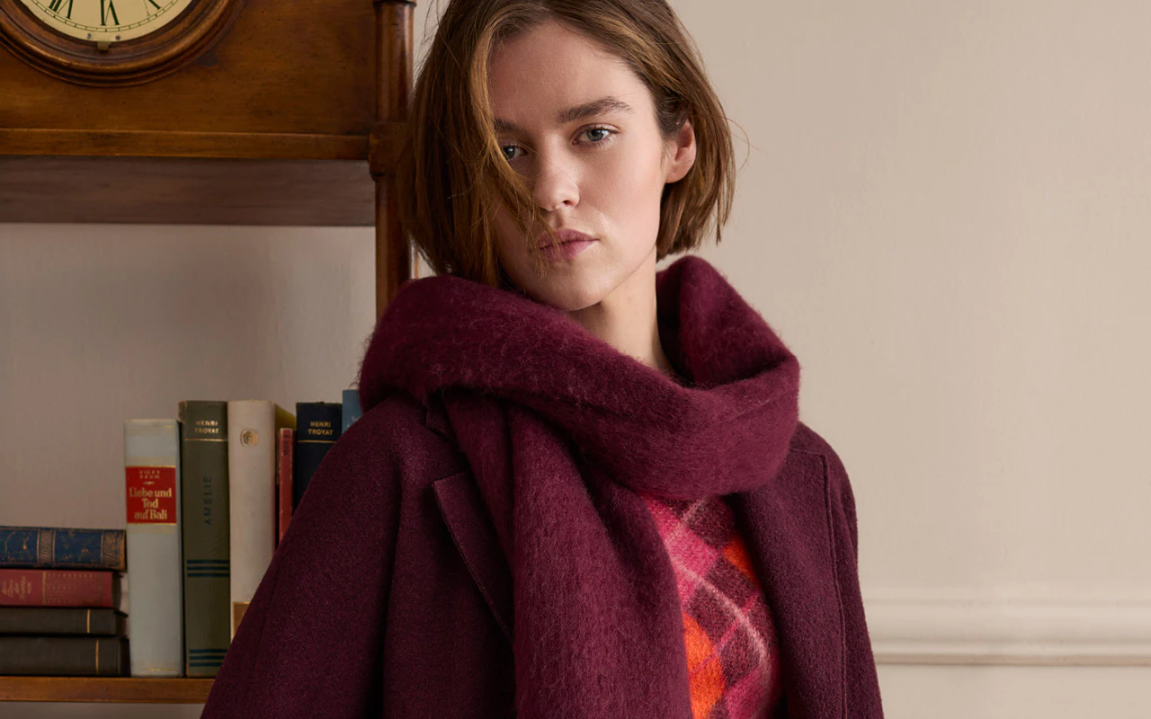 A burgundy coat with a matching scarf, paired with a checked knitted jumper in bright shades of pink and orange.