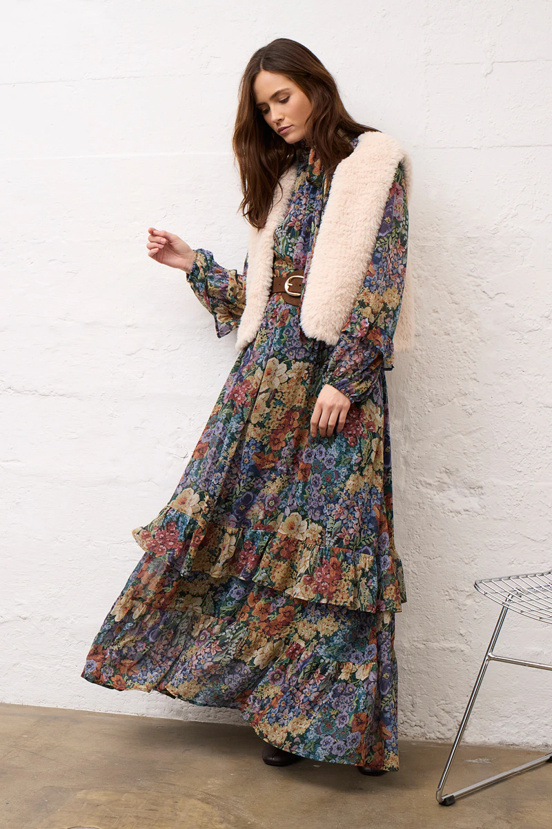 A woman wearing a floral midi dress and a beige waistcoat.