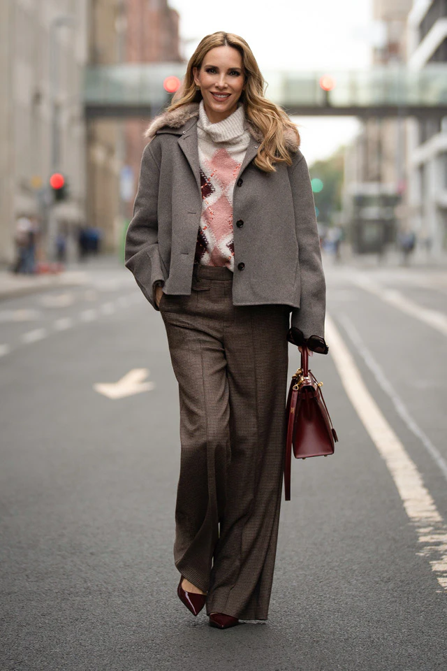 Alexandra Lapp is wearing a grey coat, a patterned jumper and checked trousers, and is walking through the city with a burgundy handbag.