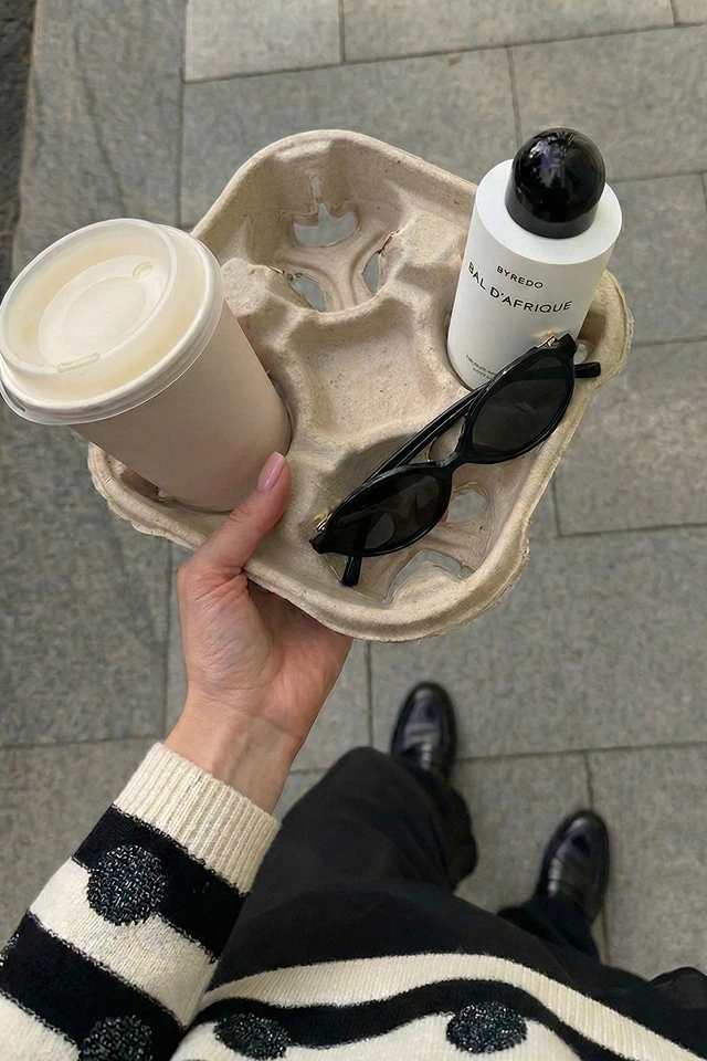 Ein Bild von oben aufgenommen, zeigt eine Hand mit einem Pullover aus schwarzen und weissen Streifen mit Pailletten Punkte in schwarz, einen schwarzen Rock und die Hand trägt einen Kaffebecher.