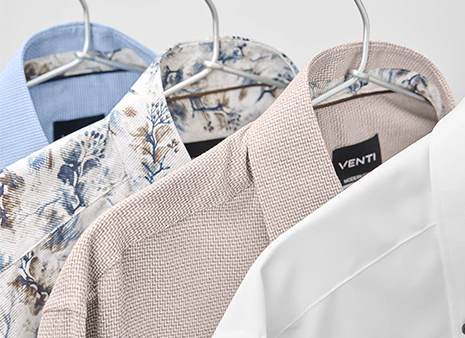 Businesshemden in Weiß, Beige, Blau und mit floralem Muster hängen auf Bügeln.