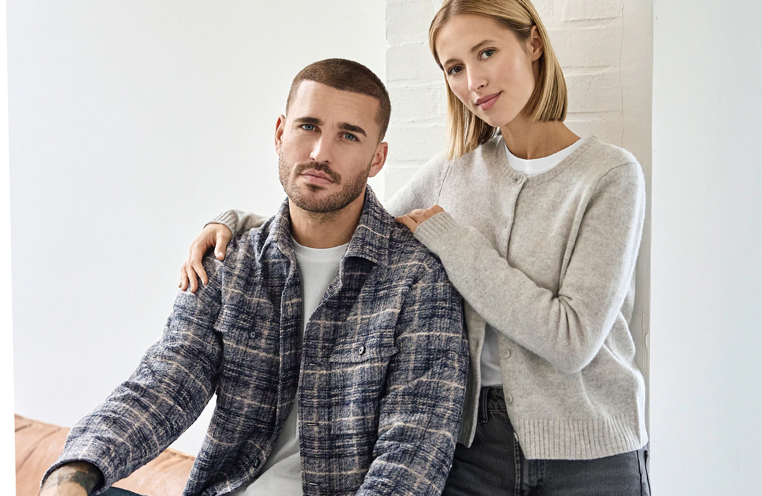Ein Model trägt ein blau-beige kariertes Overshirt über weißem T-Shirt, neben einer Frau im hellgrauen Cardigan.