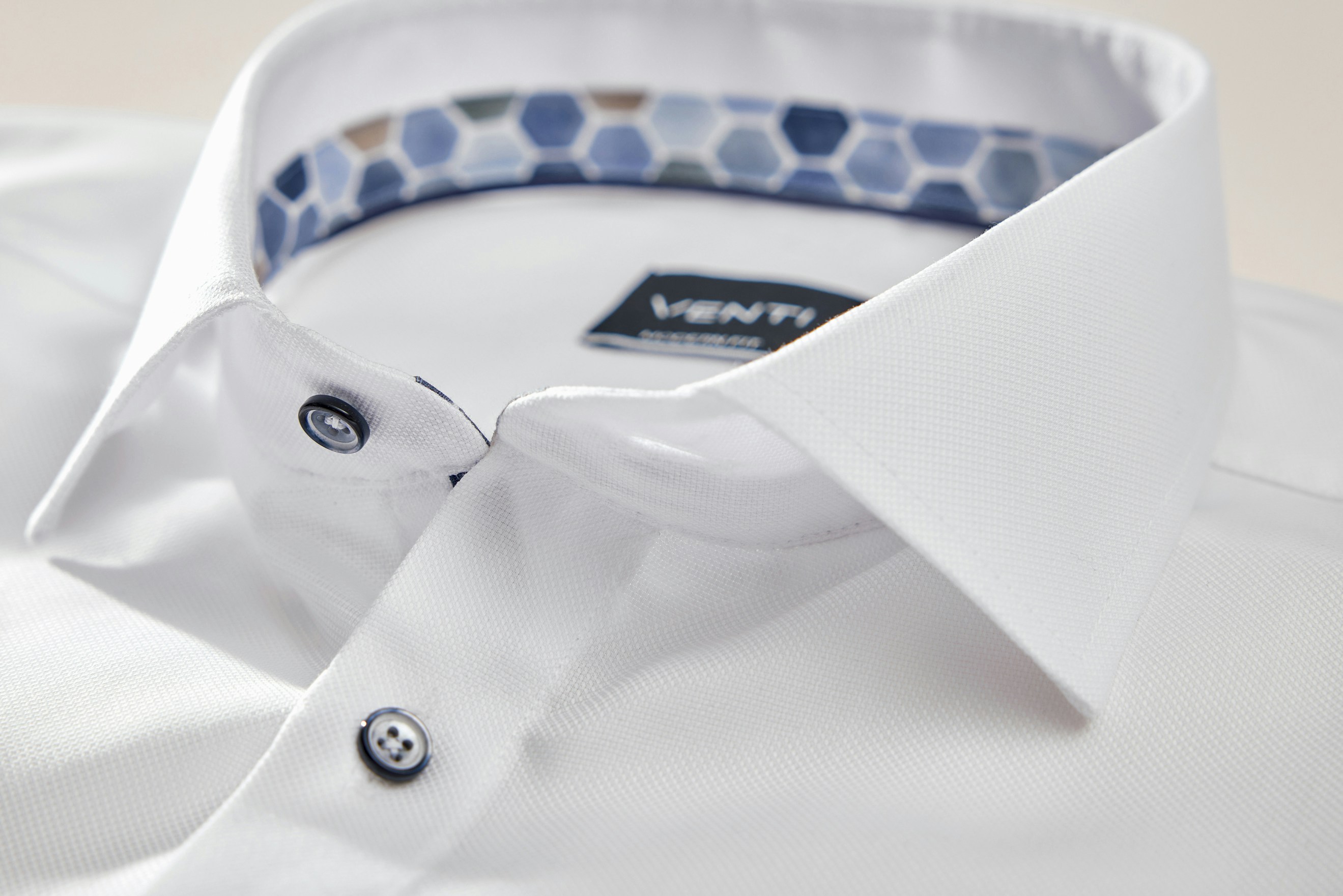 Detailaufnahme eines weißen Hemdes mit klassischem Kragen, sichtbaren Knöpfen und gemustertem Innenkragen in Blau- und Beigetönen mit VENTI-Label