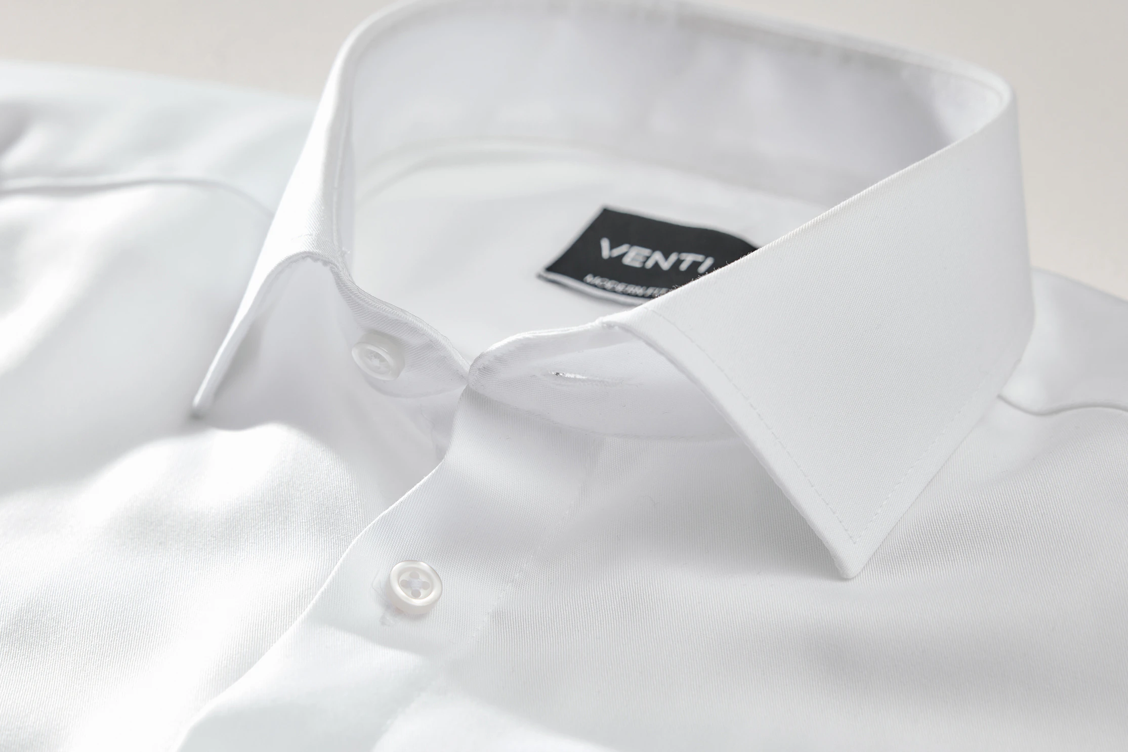 Detailaufnahme eines weißen Hemdes mit klassischem Kragen, sichtbaren Knöpfen und eingenähtem VENTI-Label