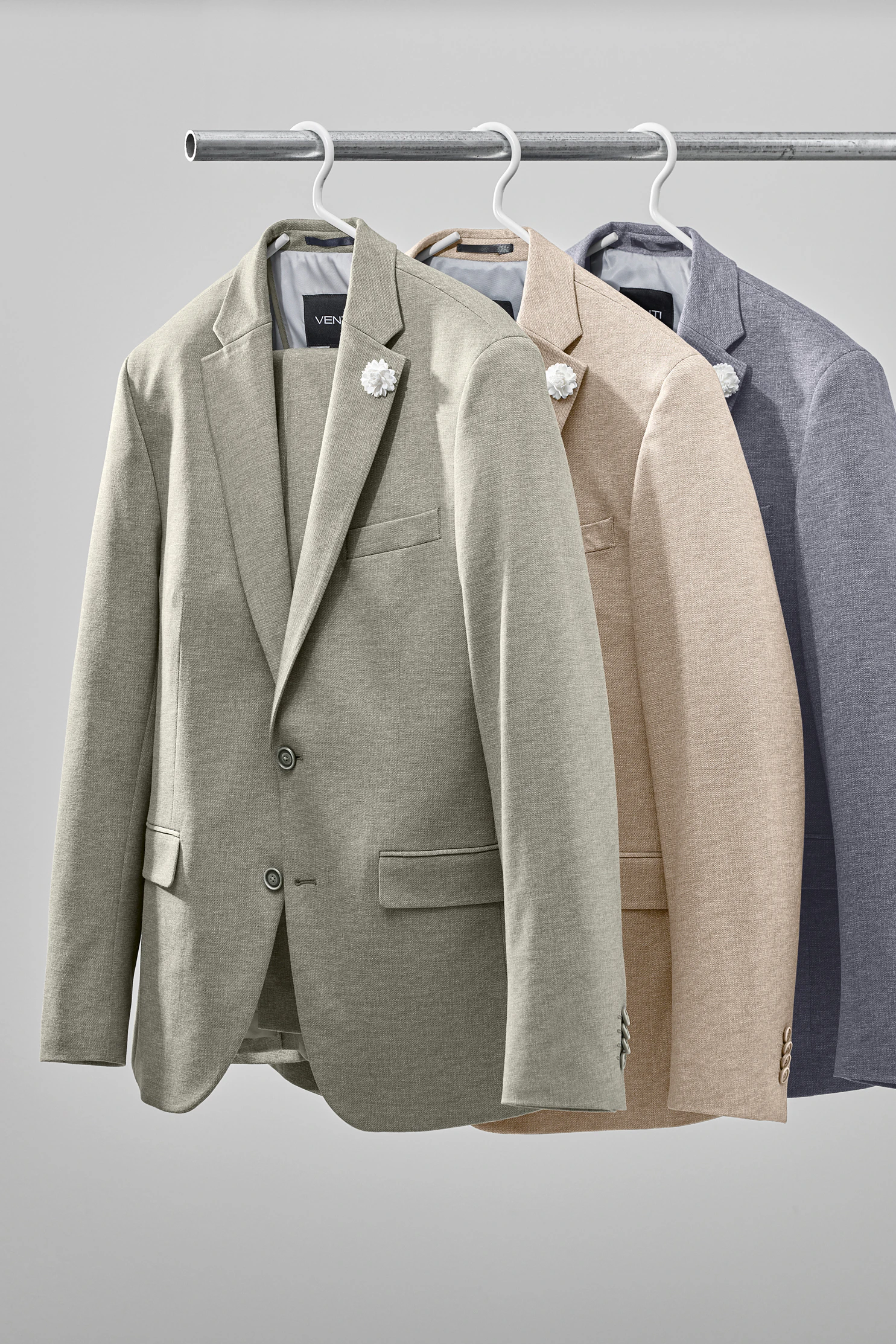 Mehrere Herrenanzug-Sakkos in Grün-, Beige- und Grautönen hängen nebeneinander auf einer Kleiderstange