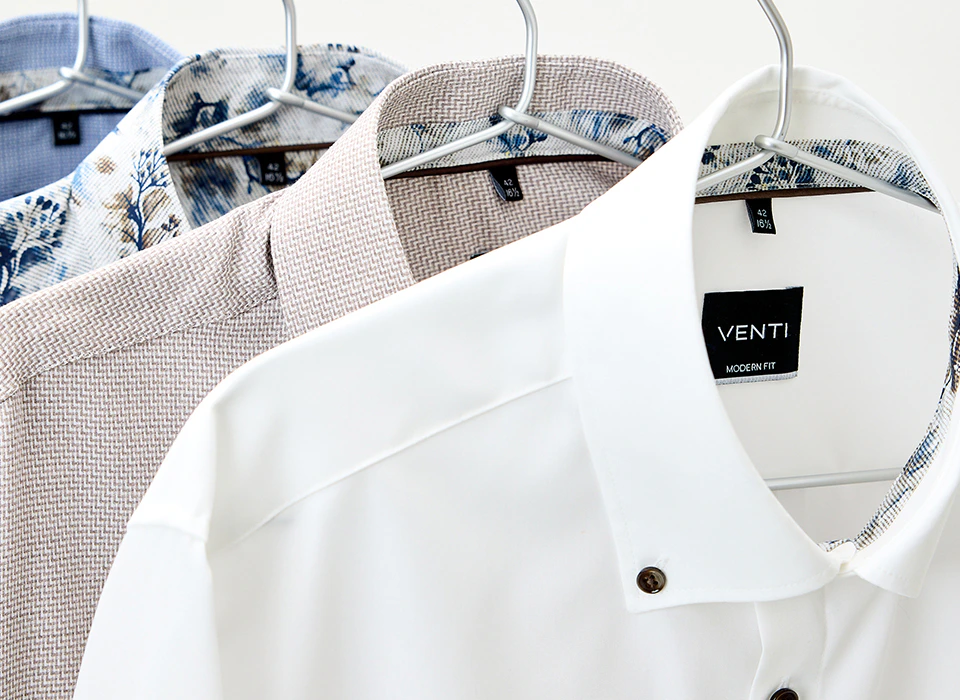 Businesshemden in Weiß, Beige, Blau und mit floralem Muster hängen auf Bügeln.