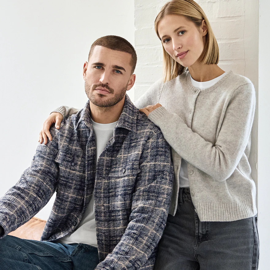 Ein Model trägt ein blau-beige kariertes Overshirt über weißem T-Shirt, neben einer Frau im hellgrauen Cardigan.