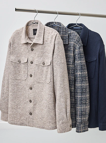 Drei Herren-Overshirts in Beige, Blau kariert und Dunkelblau hängen auf einer Kleiderstange.