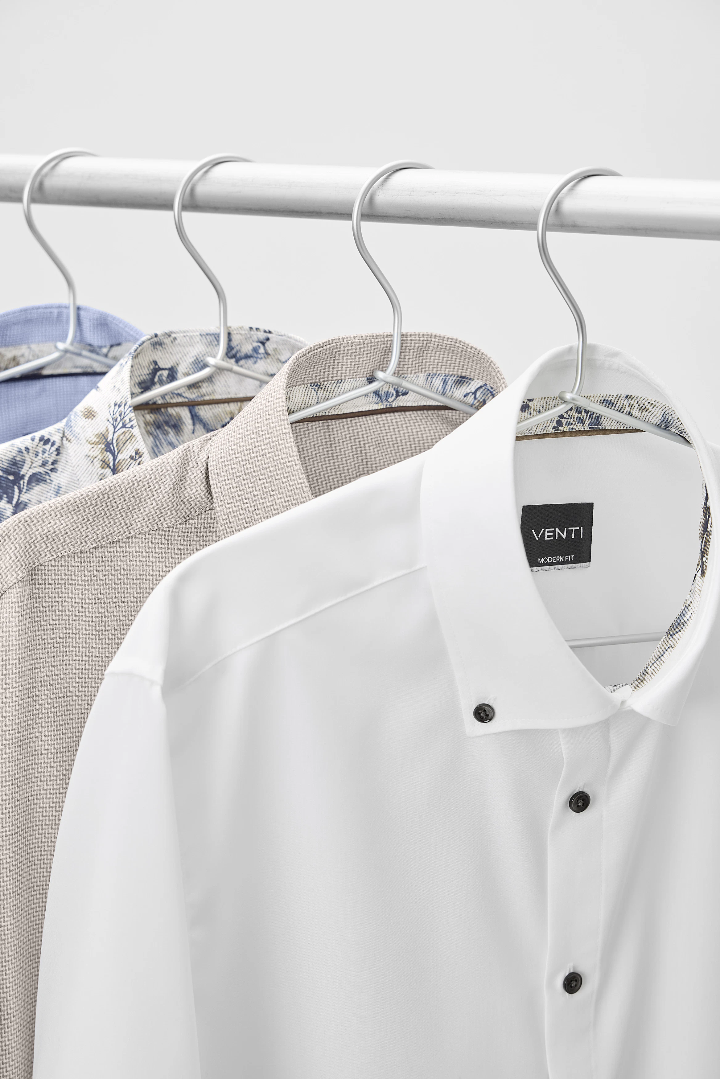 Businesshemden in Weiß, Beige, Blau und mit floralem Muster hängen auf Bügeln.