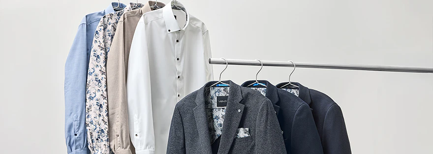 Businesshemden und Sakkos in Blau, Weiß und Beige auf Kleiderstangen.